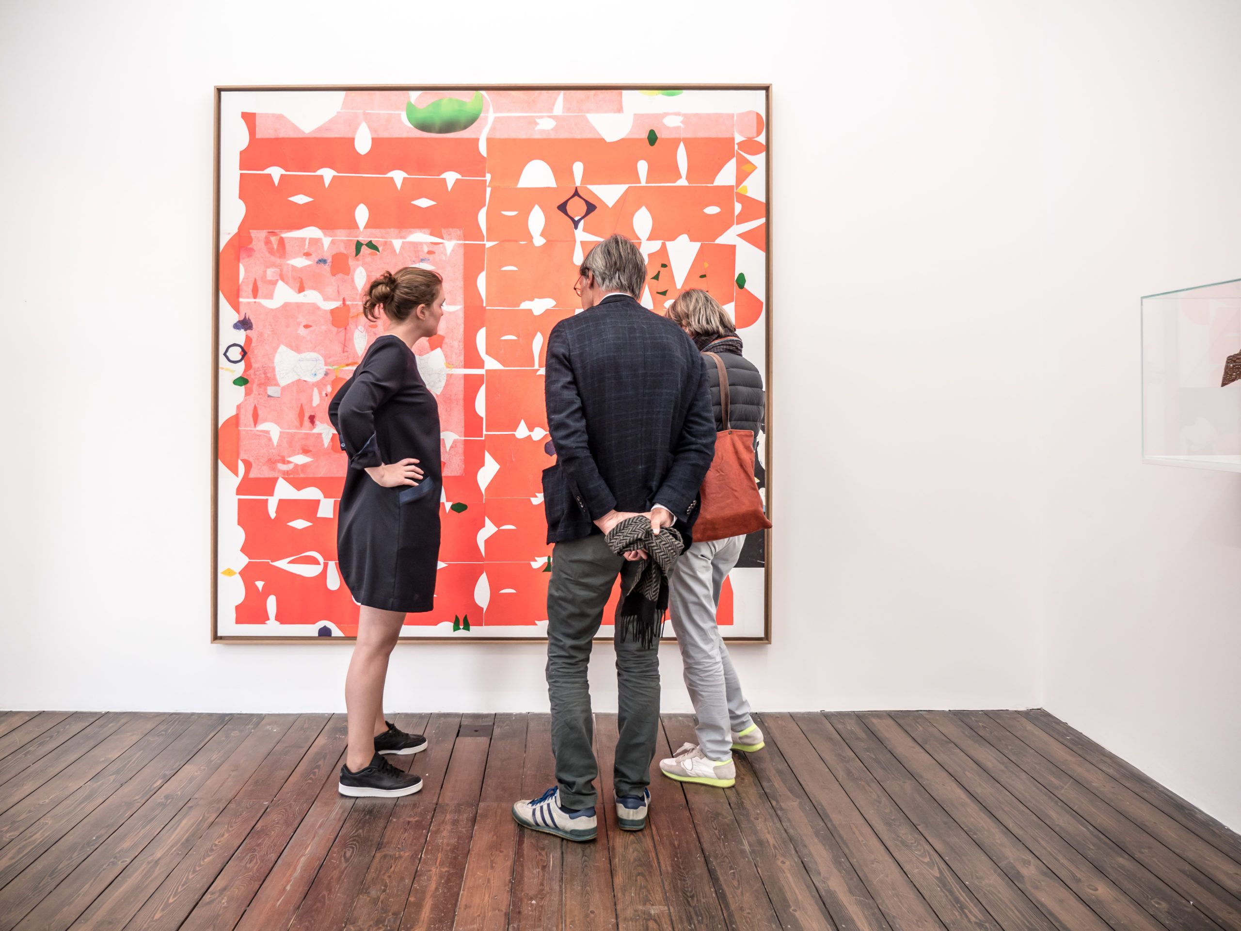 Trois personnes devant un tableau abstrait de couleur rouge