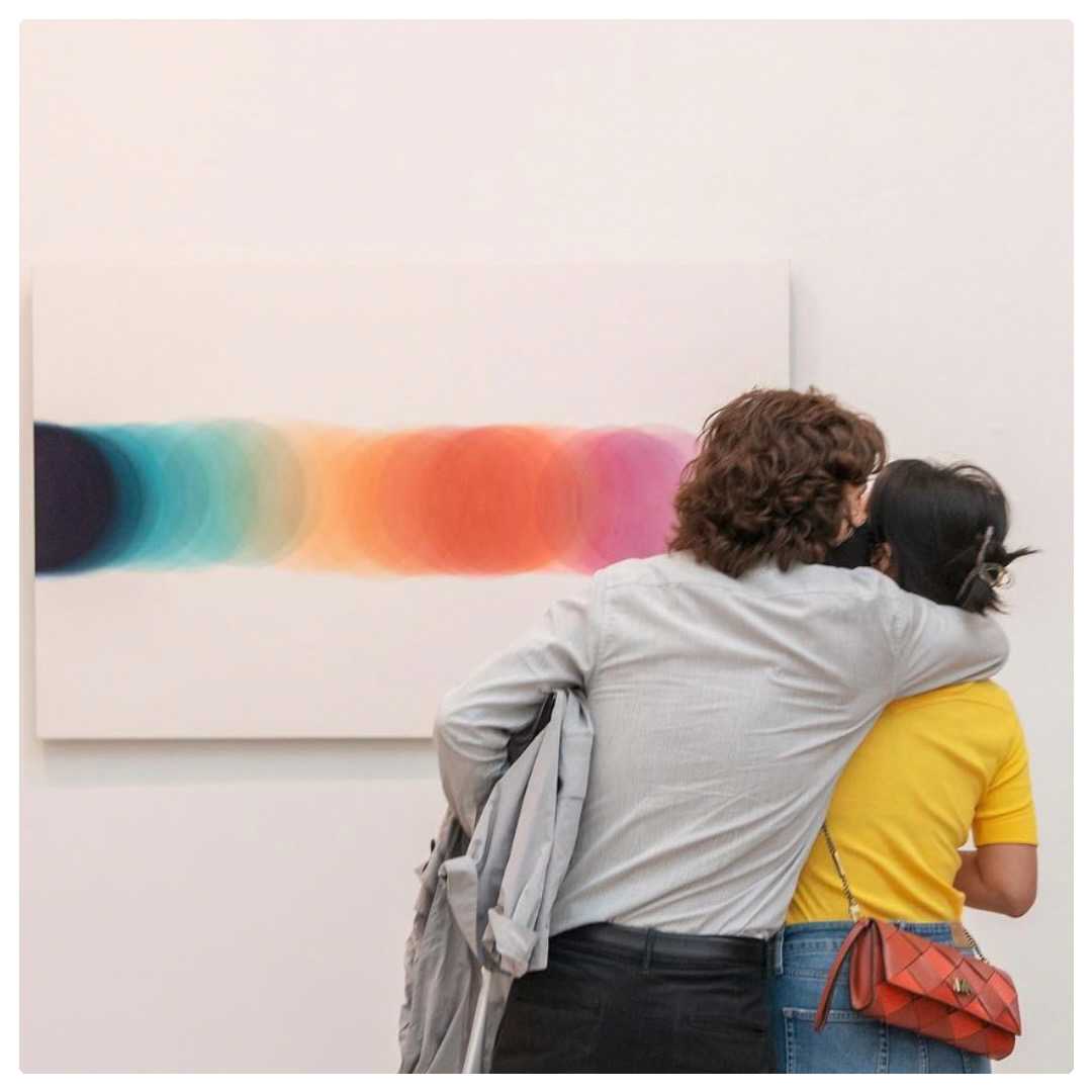 couple se prenant par les épaules devant un tableau avec des ronds colorés.